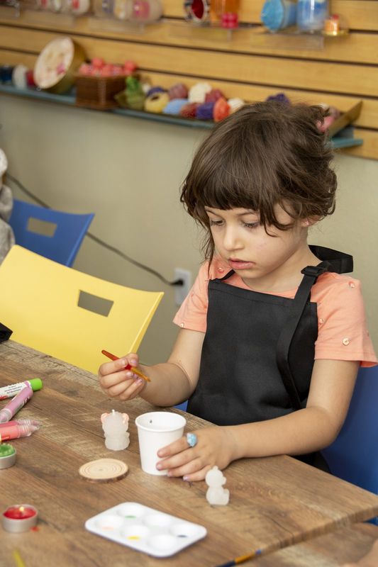 A girl in a black apron painting her candle